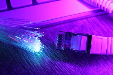 Photo of Optical fiber strands transmitting different color lights near cable with modular connector and computer keyboard on table, closeup