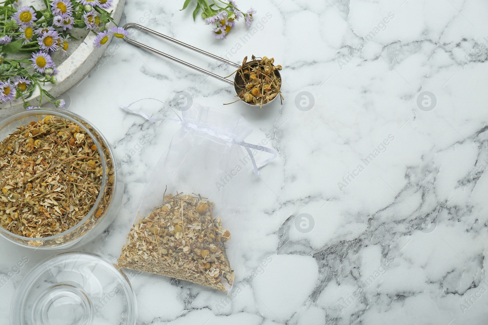 Photo of Scented sachet and dried chamomile flowers on white marble table, flat lay. Space for text