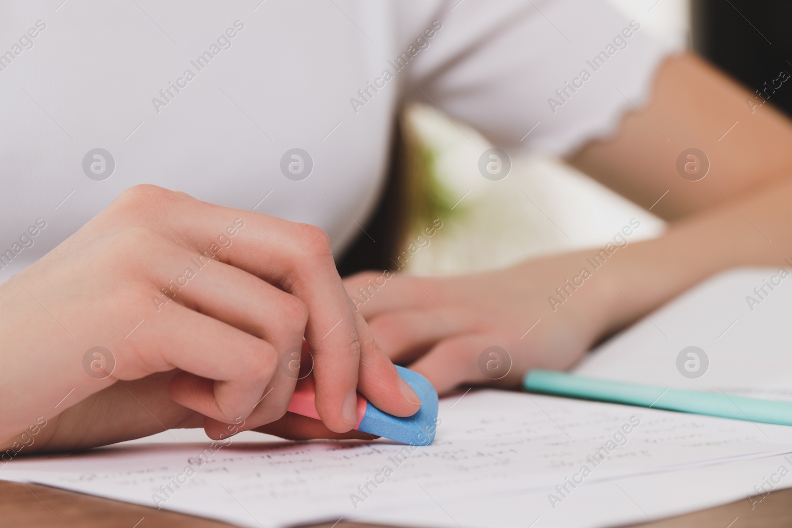 Photo of Girl erasing mistake in her notebook at wooden desk, closeup