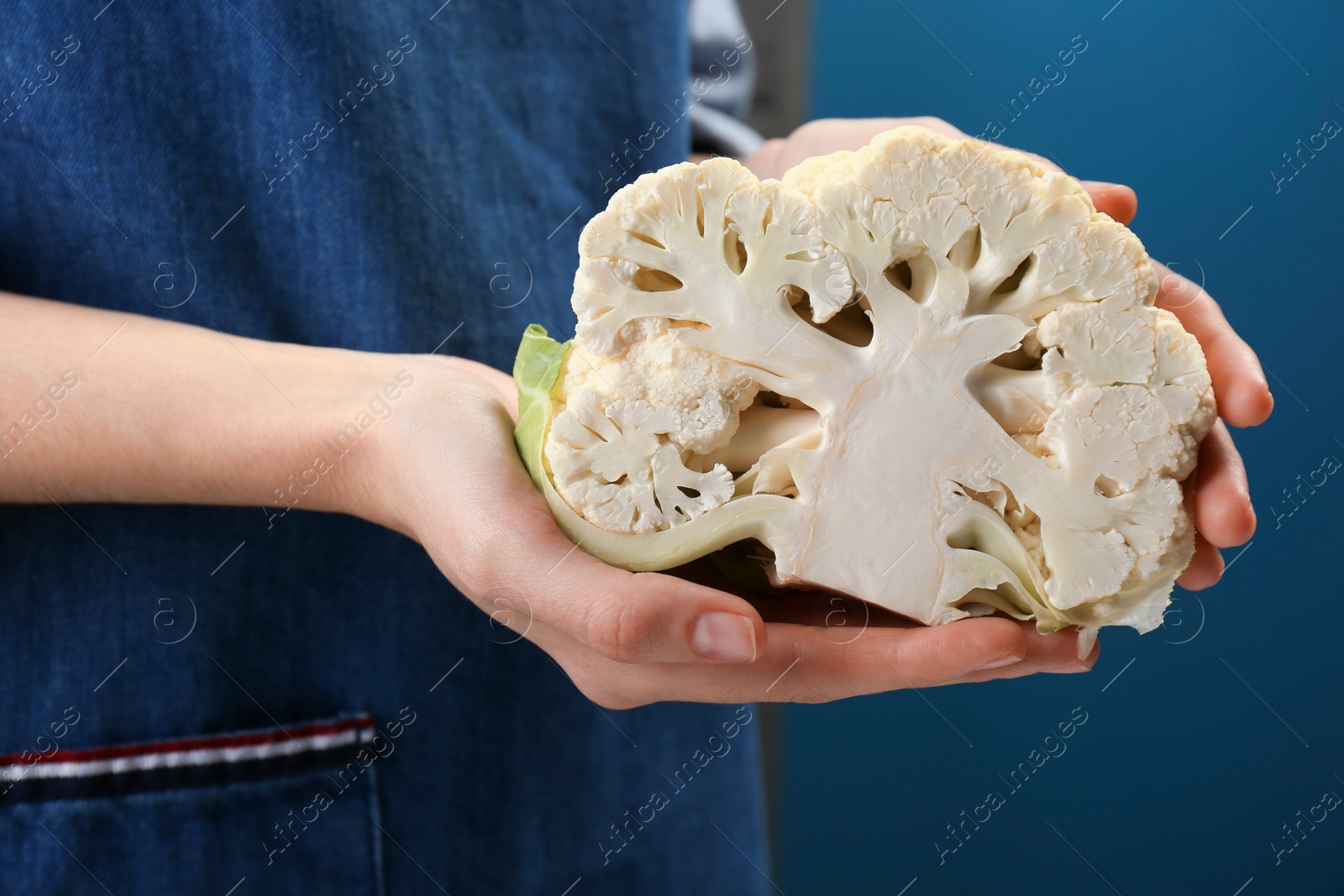 Photo of Woman holding fresh cauliflower against dark blue background, closeup