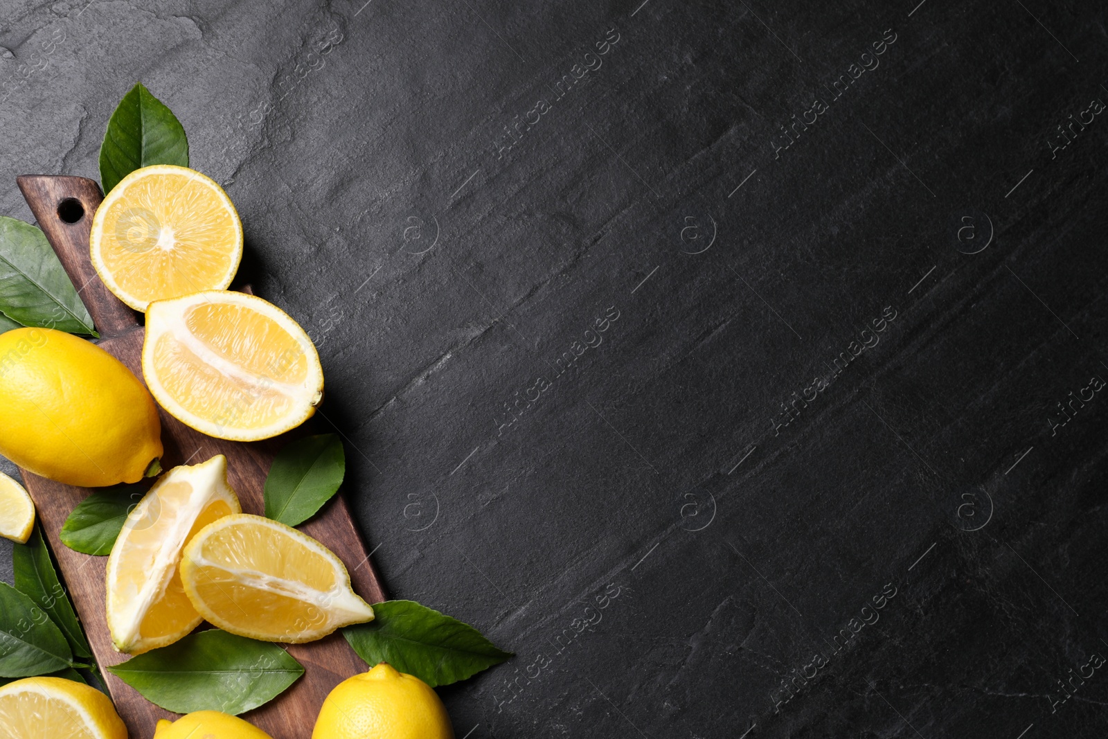 Photo of Many fresh ripe lemons with green leaves on black table, top view. Space for text