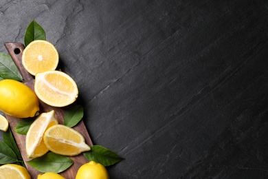 Many fresh ripe lemons with green leaves on black table, top view. Space for text