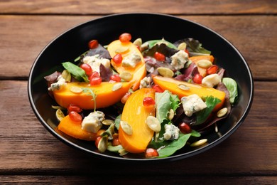 Photo of Delicious persimmon salad with pomegranate and spinach on wooden table
