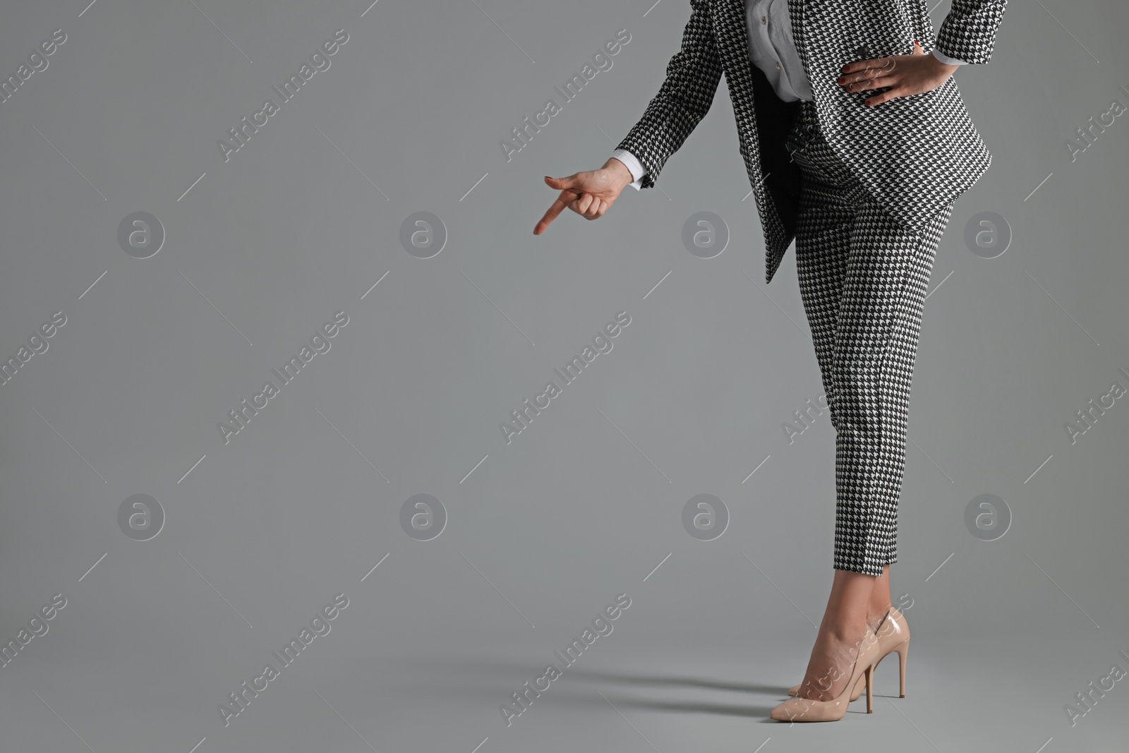 Photo of Businesswoman in beige shoes pointing at something on grey background, closeup. Space for text