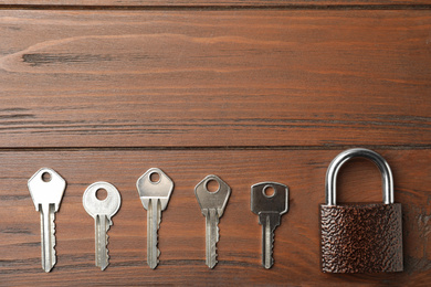 Photo of Steel padlock and keys on wooden background, flat lay with space for text. Safety concept