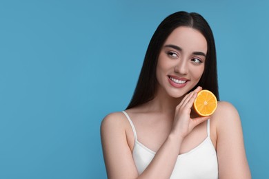 Beautiful young woman with piece of orange on light blue background. Space for text