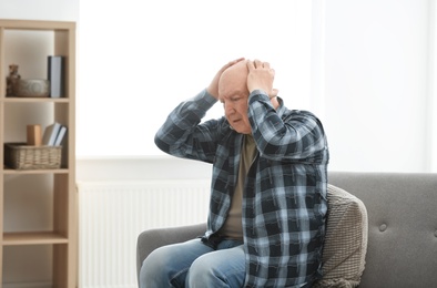 Photo of Depressed senior man sitting on sofa indoors