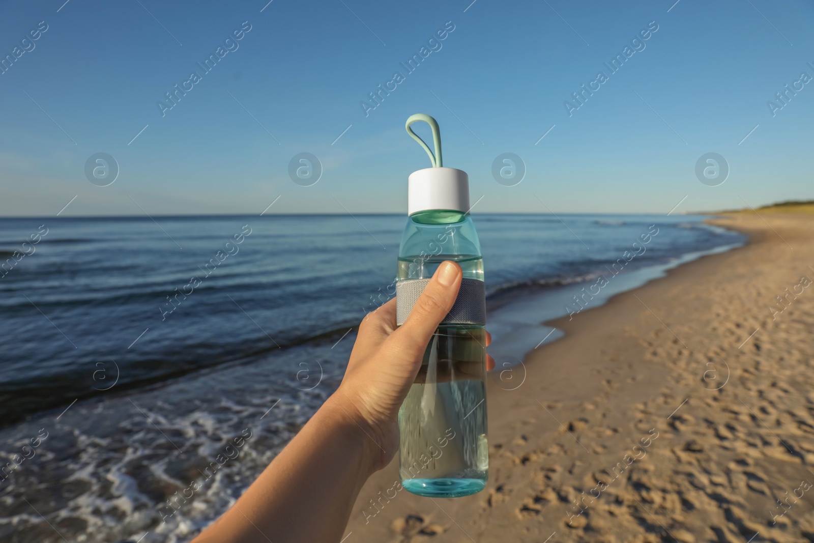 Photo of Woman holding glass bottle with water near sea, closeup