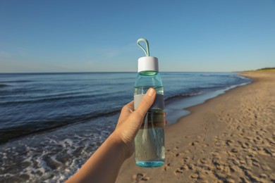 Woman holding glass bottle with water near sea, closeup