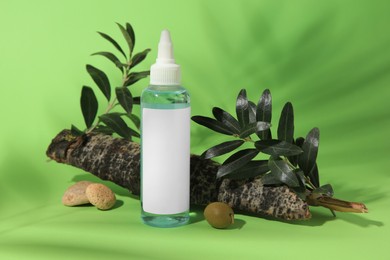 Bottle of cosmetic product, olives and leaves on light green background