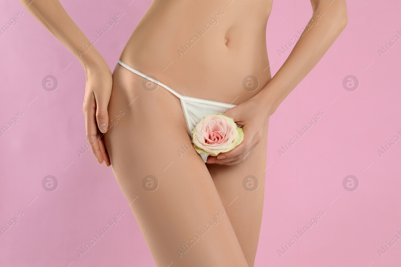 Photo of Woman with flower showing smooth skin after Brazilian bikini epilation on pink background, closeup. Body care concept