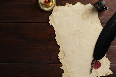 Photo of Sheet of old parchment paper with wax stamp, black feather, inkwell and candle on wooden table, flat lay. Space for text