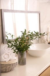 Photo of Vase with beautiful branches and fresh towels near vessel sink in bathroom. Interior design