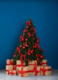 Photo of Decorated Christmas tree and gift boxes near blue wall