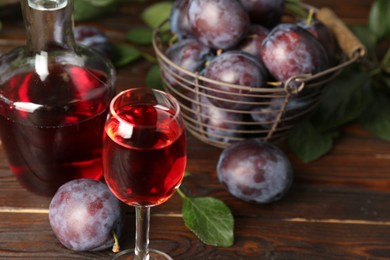 Photo of Delicious plum liquor and ripe fruits on wooden table. Homemade strong alcoholic beverage