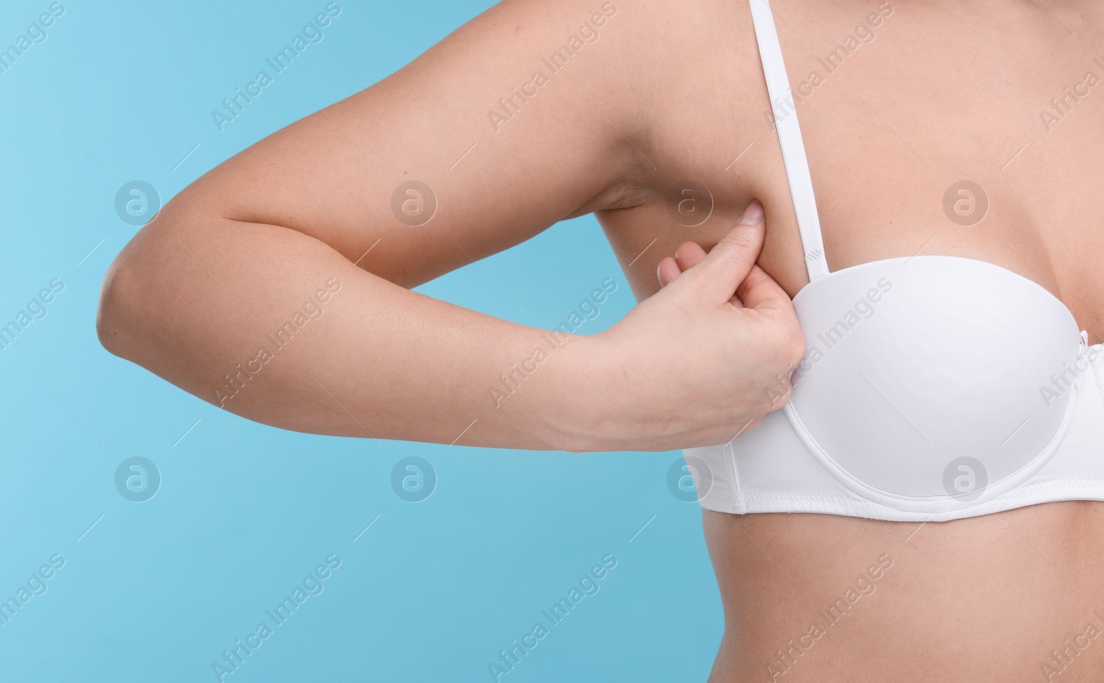 Photo of Mammology. Woman in bra doing breast self-examination on light blue background, closeup