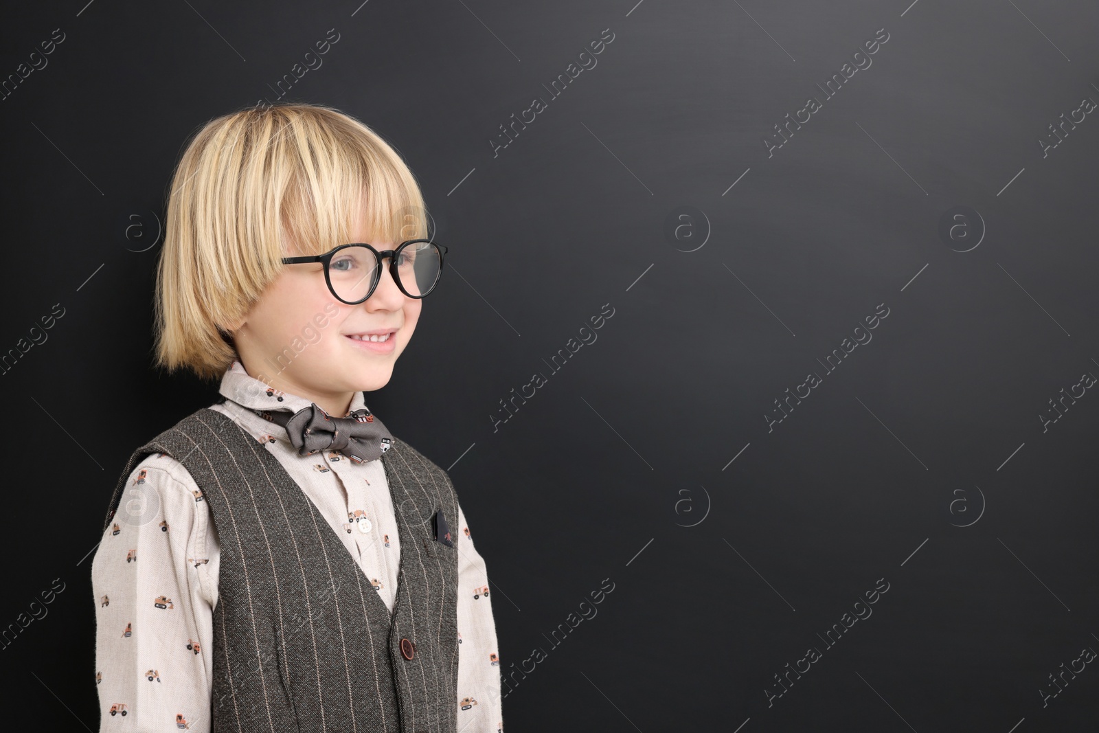 Photo of Happy little school child in uniform near chalkboard. Space for text