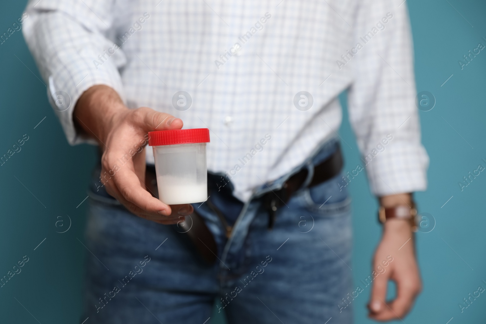 Photo of Donor with unzipped pants holding container of sperm on turquoise background, closeup