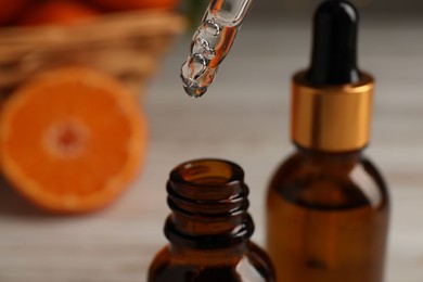 Photo of Tangerine essential oil dripping from pipette into bottle on blurred background, closeup