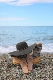 Photo of Beautiful hat, bag and flip flops near sea on pebble beach