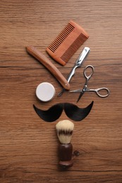 Photo of Artificial moustache and barber tools on wooden table, flat lay