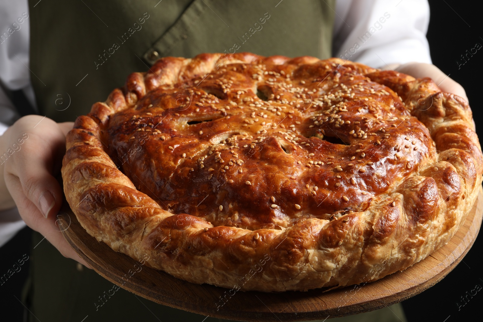 Photo of Woman holding tasty homemade pie on black background, closeup