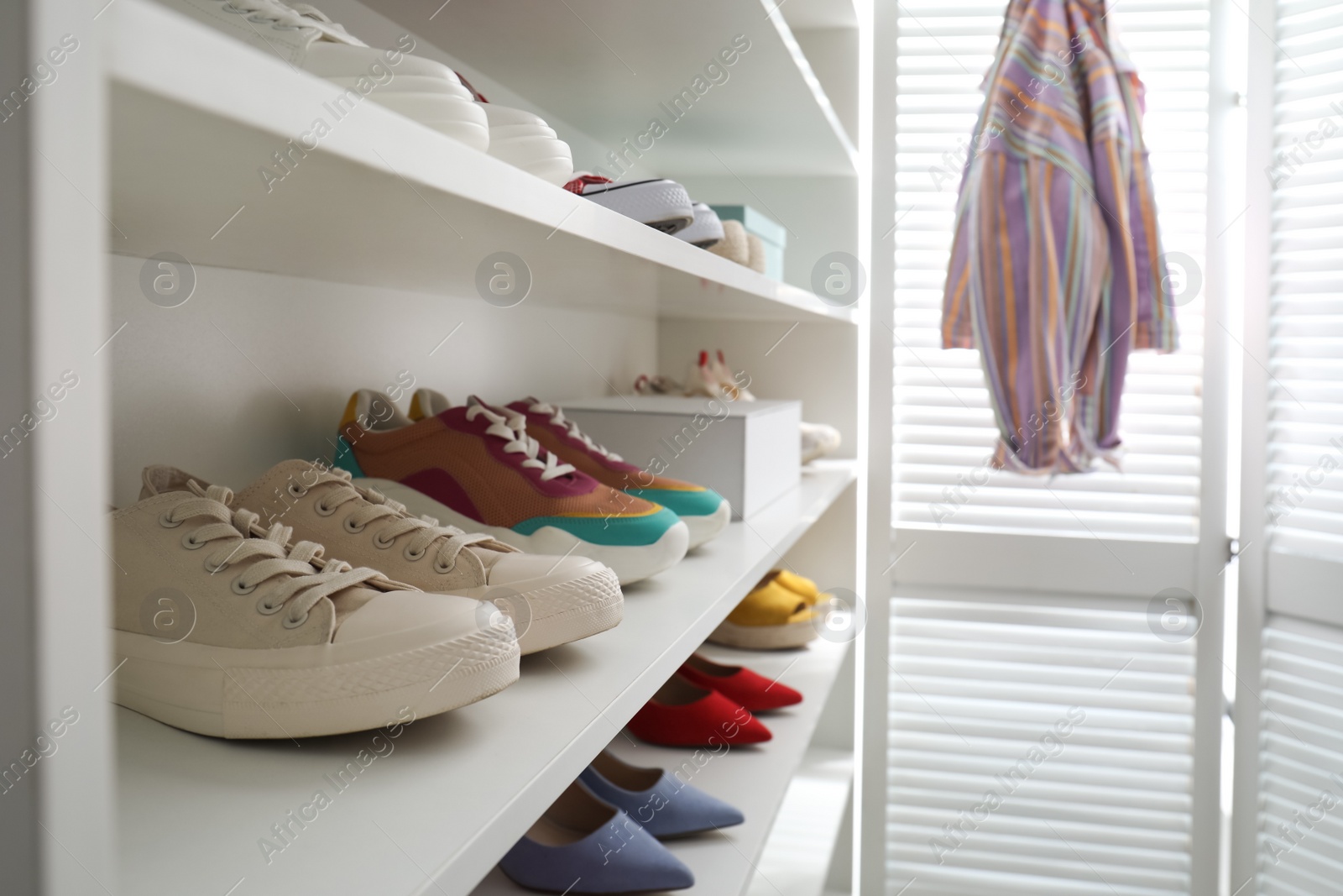 Photo of White shelving unit with collection of colorful sneakers indoors