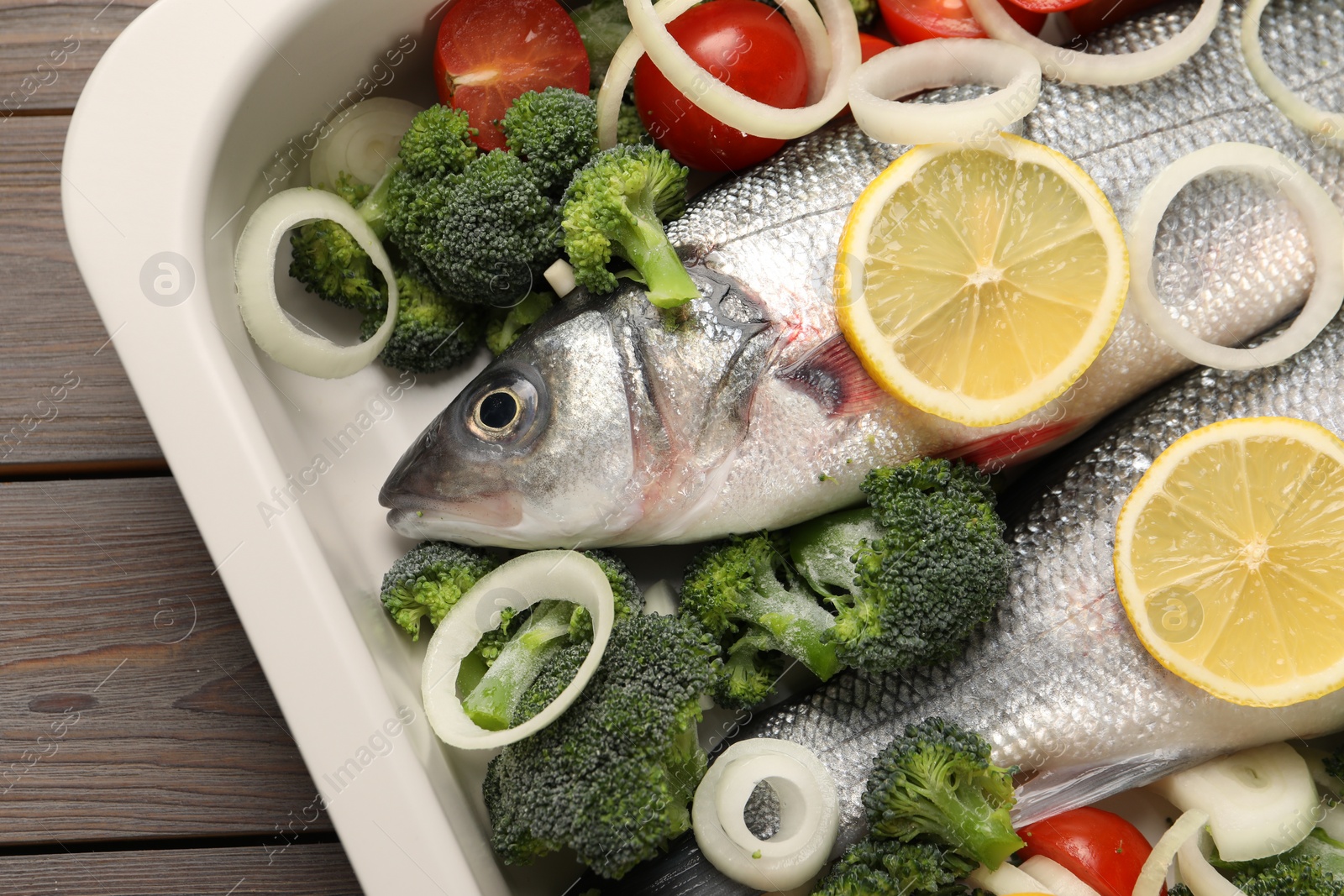 Photo of Raw fish with vegetables and lemon in baking dish on wooden table, top view