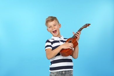 Portrait of emotional little boy playing guitar on color background