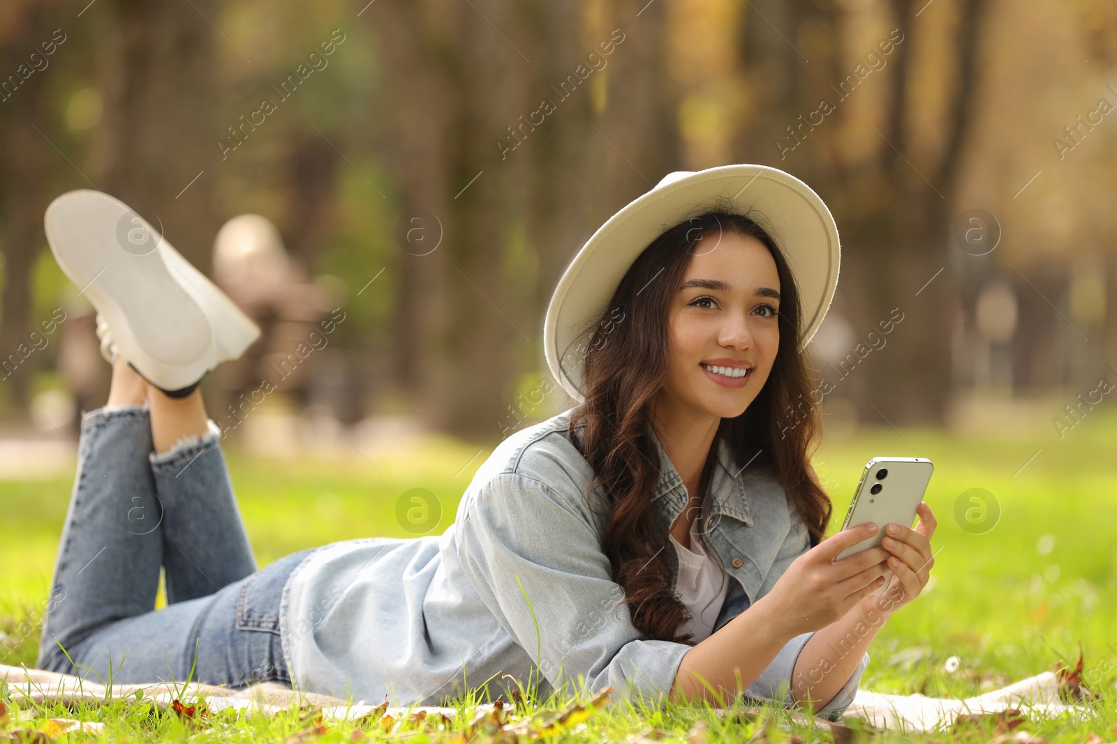 Photo of Young woman lying on green grass and using smartphone in park