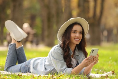Photo of Young woman lying on green grass and using smartphone in park