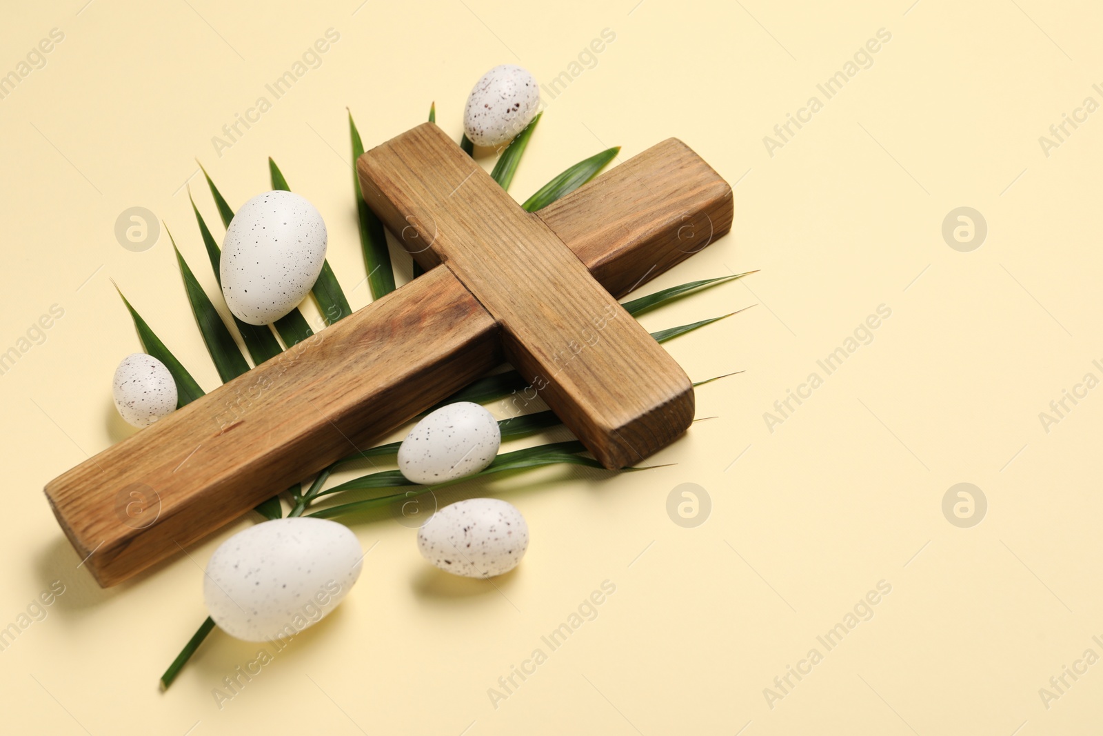 Photo of Wooden cross, painted Easter eggs and palm leaf on beige background, space for text