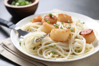 Photo of Delicious scallop pasta with green onion served on grey table, closeup