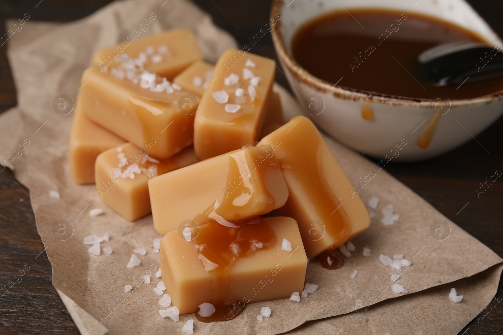 Photo of Delicious candies with sea salt and caramel sauce on wooden table, closeup