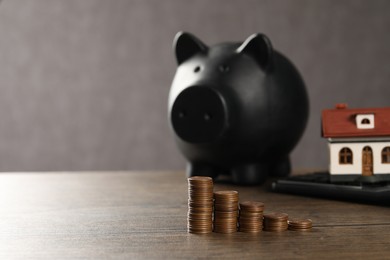 Photo of House model, piggy bank, calculator and stacked coins on wooden table, selective focus. Space for text