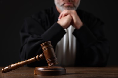 Judge with gavel sitting at wooden table against black background, closeup