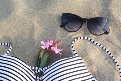 Beautiful sunglasses, swimsuit and tropical flower on sand
