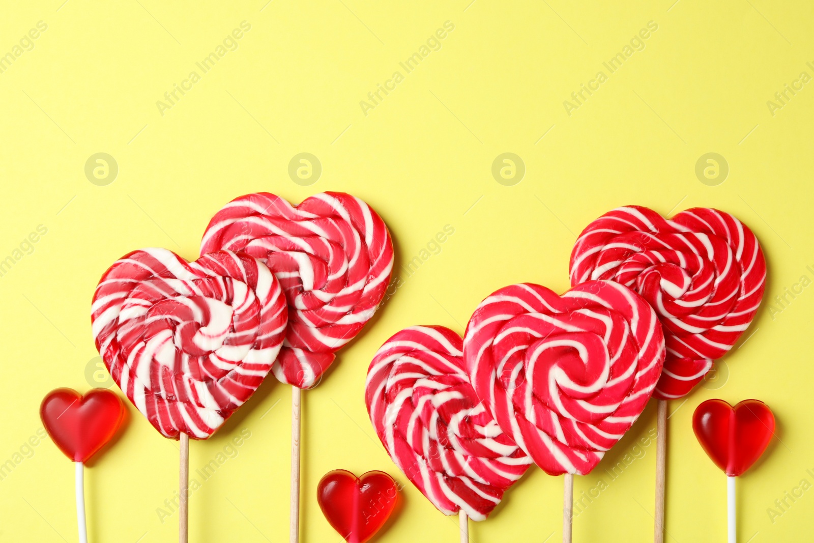 Photo of Sweet heart shaped lollipops on yellow background, flat lay with space for text. Valentine's day celebration