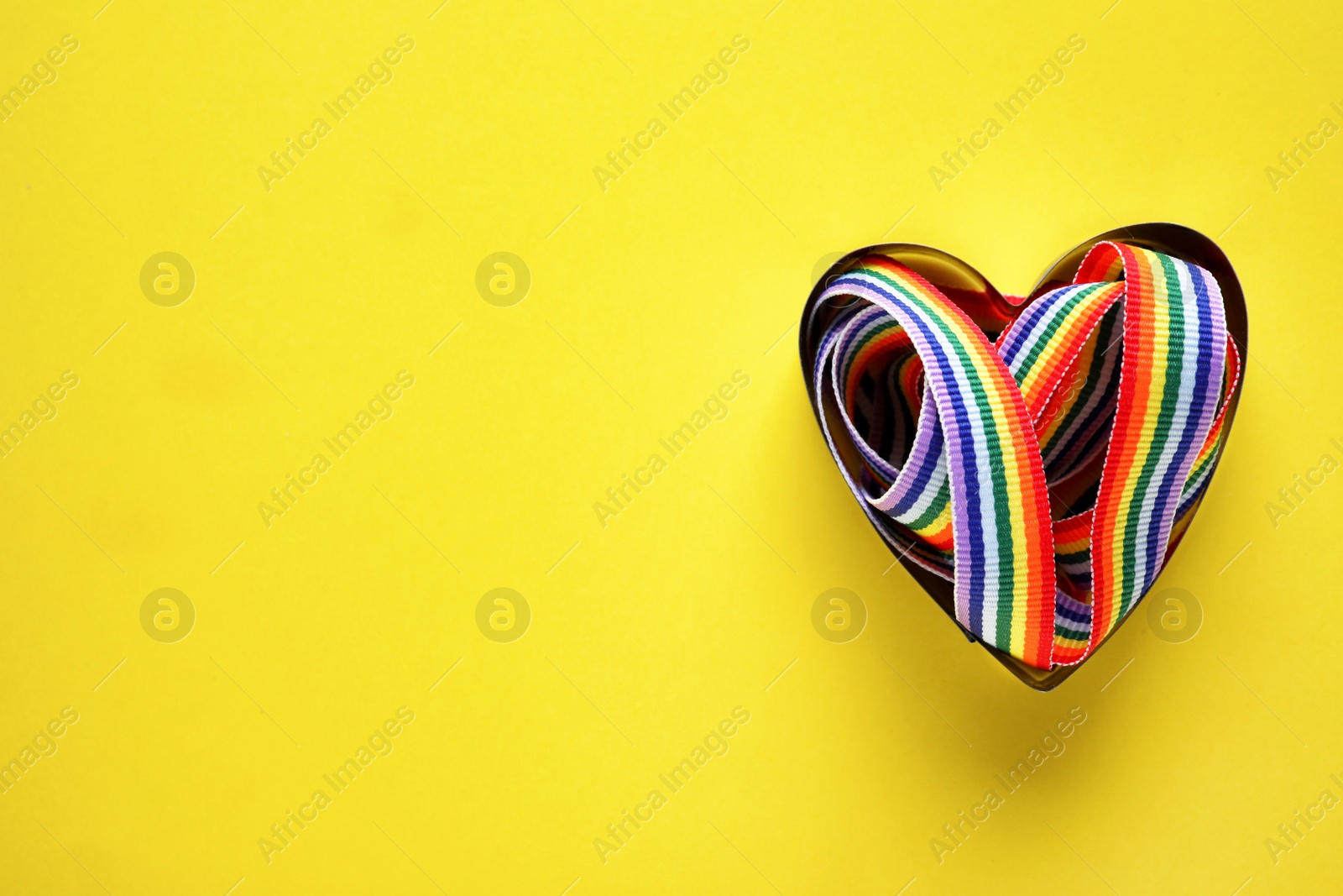 Photo of Top view of rainbow ribbon in heart shaped box on yellow background, space for text. Gay symbol