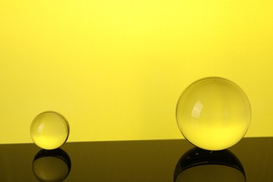 Photo of Transparent glass balls on mirror surface against yellow background. Space for text
