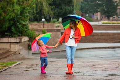 Photo of Happy mother and daughter with bright umbrella under rain outdoors