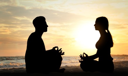 Image of Silhouette of lovely couple meditating together on beach at sunset