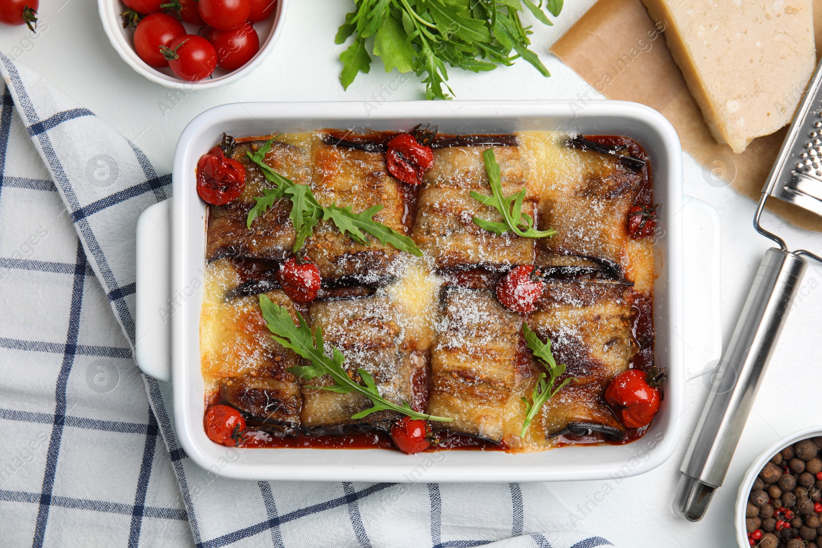 Photo of Tasty eggplant rolls with tomatoes, cheese and arugula in baking dish on white table, flat lay