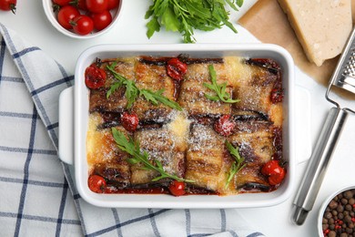 Tasty eggplant rolls with tomatoes, cheese and arugula in baking dish on white table, flat lay