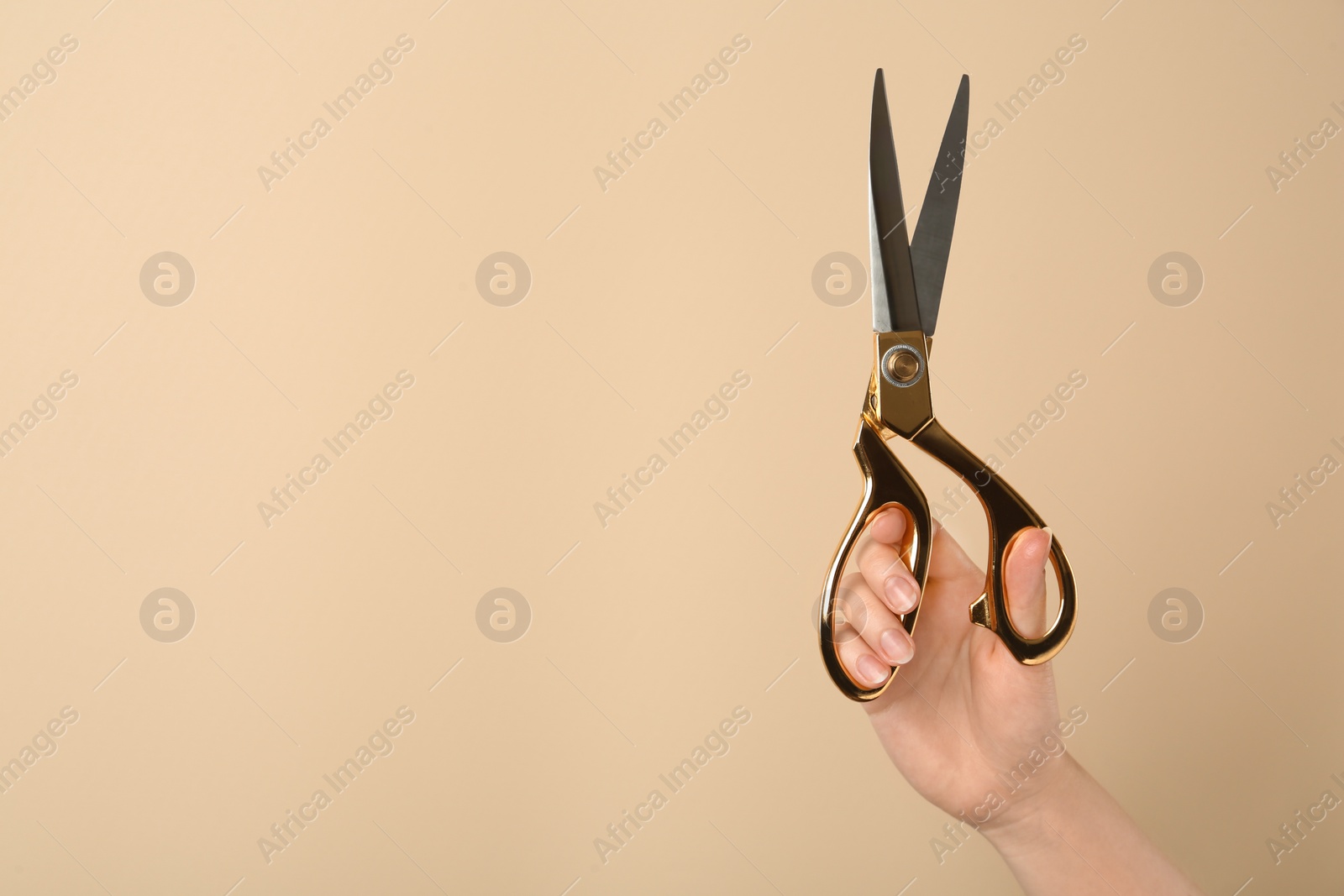 Photo of Woman holding sewing scissors on beige background, closeup. Space for text