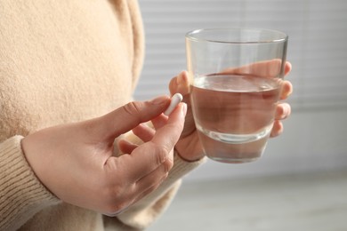 Woman with pill and glass of water on blurred background, closeup