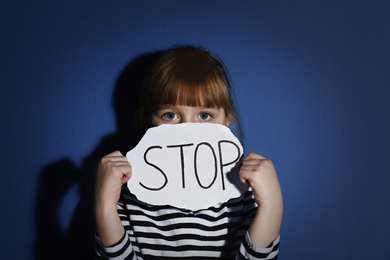 Abused little girl with sign STOP near blue wall. Domestic violence concept