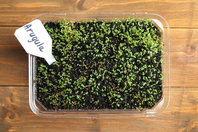 Photo of Young sprouts and card with word Arugula on wooden table, top view