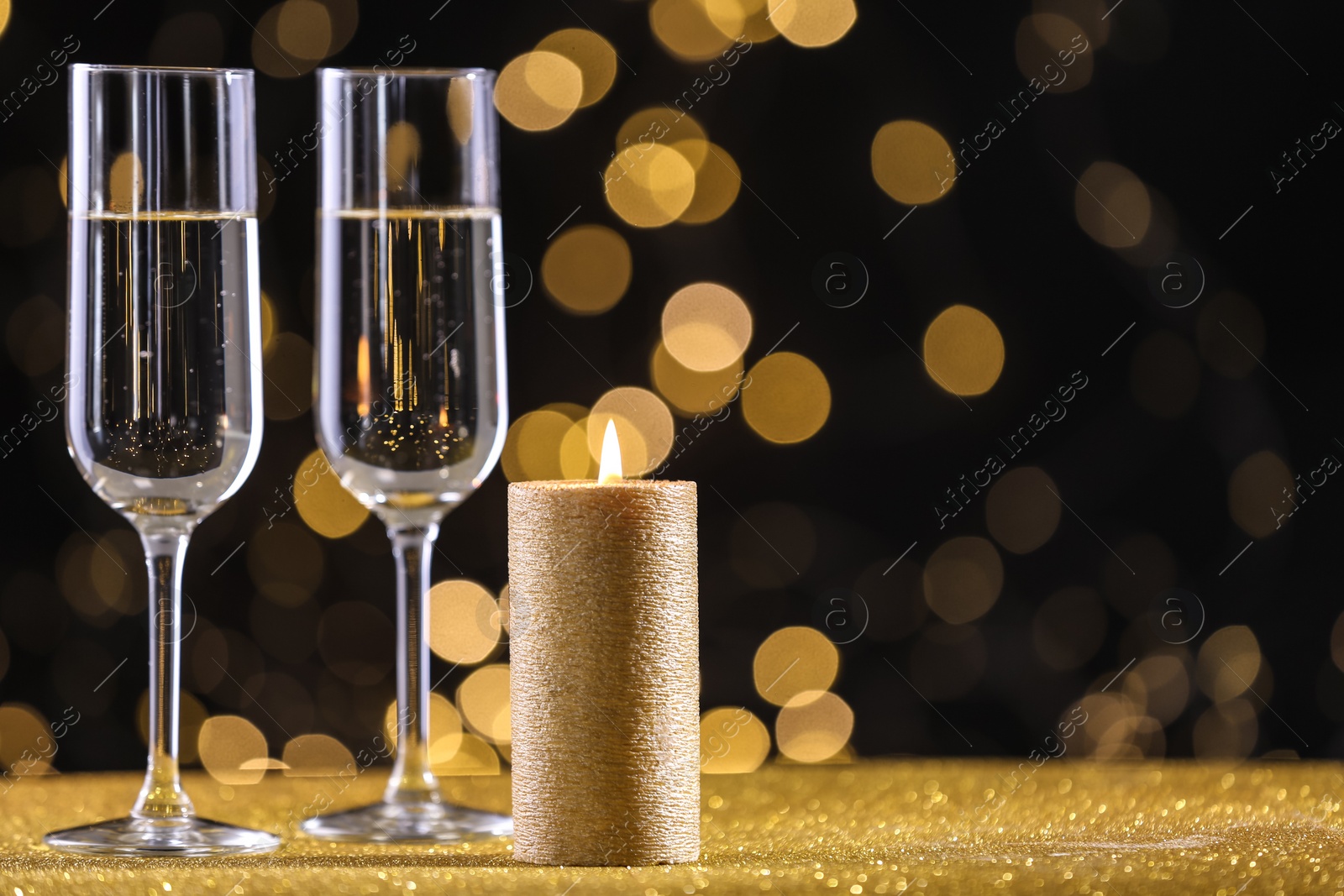 Photo of Champagne glasses and golden candle on table against defocused lights. Space for text