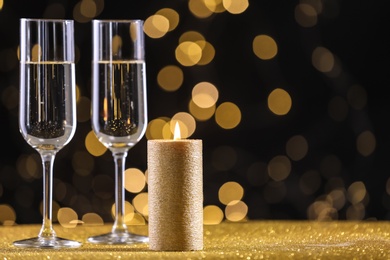 Photo of Champagne glasses and golden candle on table against defocused lights. Space for text